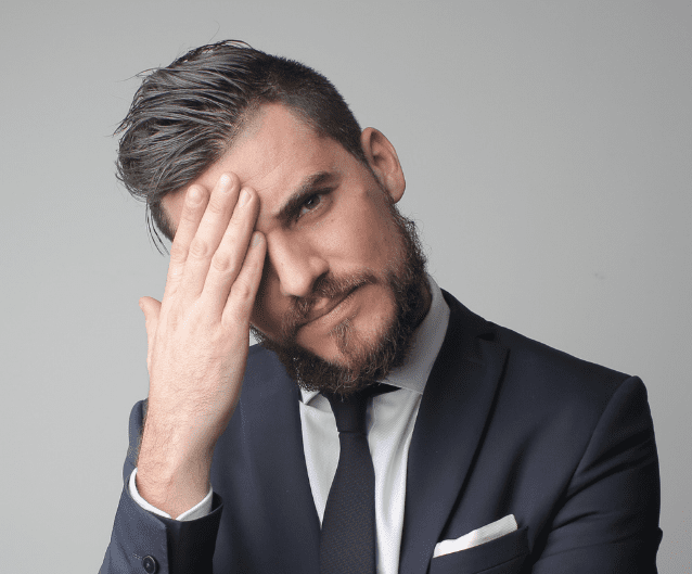 A gentleman, dressed in a suit and tie, thoughtfully touches his forehead as he considers scheduling his next appointment at Origin Dental Wellness—Tulsa's leading biological and holistic health-centered dental practice.
