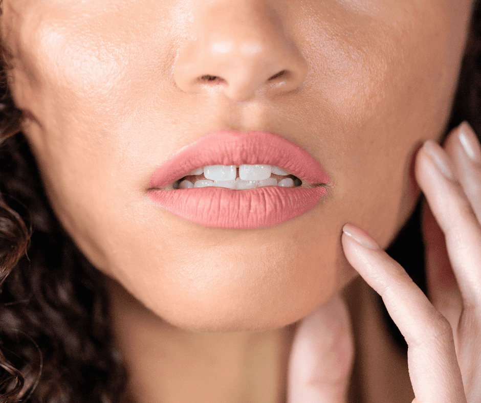 A close-up captures an individual with curly hair, gently biting the corner of their lower lip accentuated by a subtle shade of pink lipstick. With a thoughtful touch to their chin, they seem to be reflecting on their upcoming appointment with a Tulsa-based biological dentist, renowned for providing holistic dental care that emphasizes overall well-being and natural health practices.